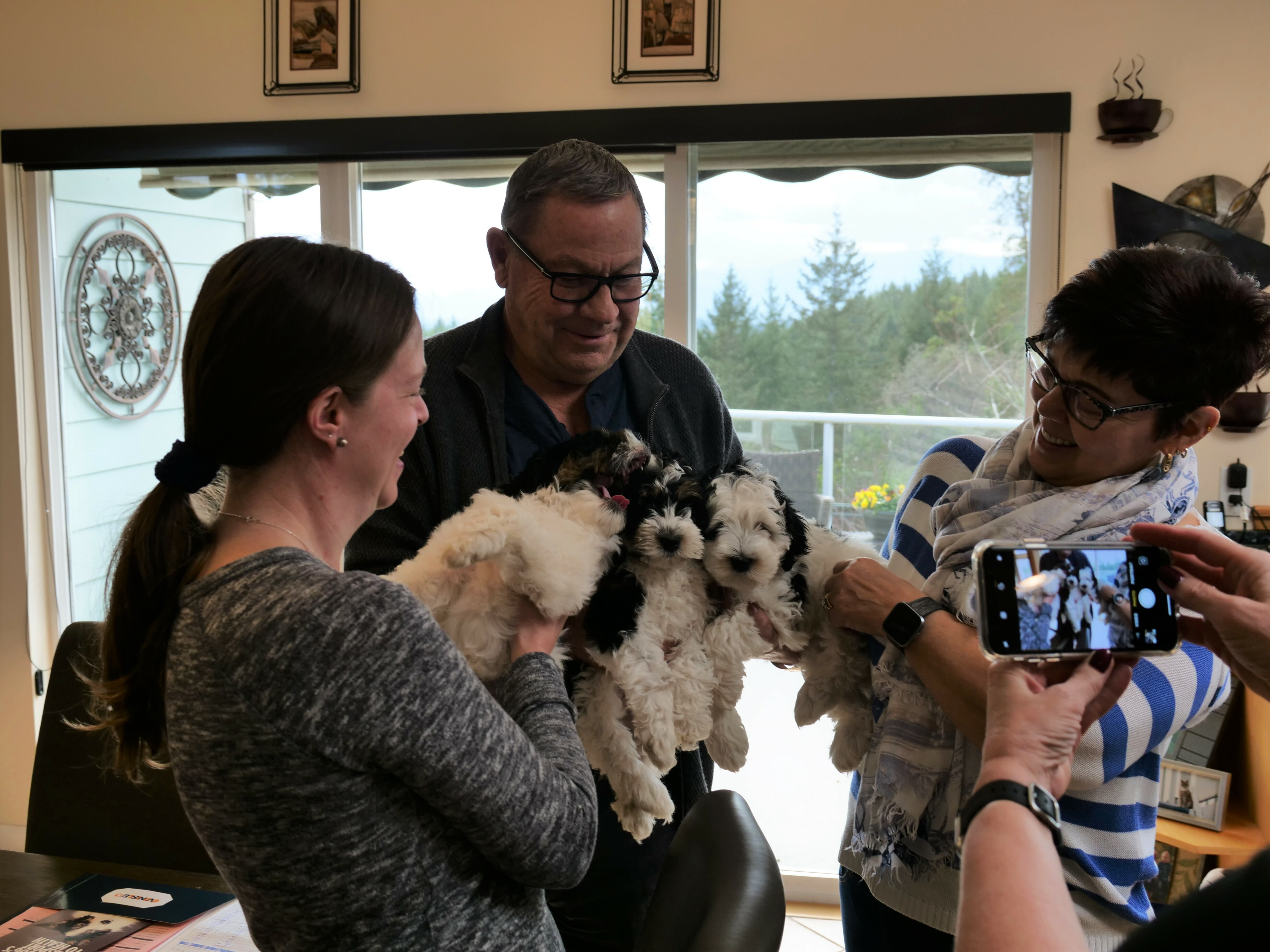 3 happy looking adults are standing close together while holding their new 8-week old black and white labradoodle puppies